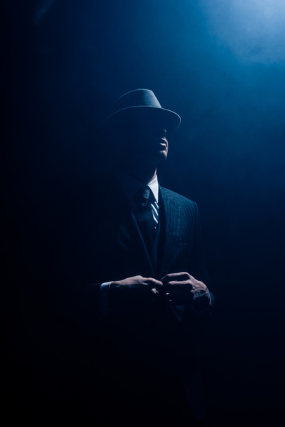 Silhouette of mafioso buttoning up on dark blue background - Foto, imagen