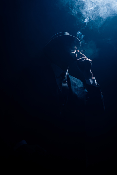 Silhouette of mafioso smoking cigarette on dark background - Foto, imagen