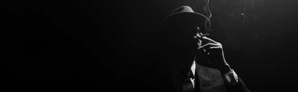 Imagen monocromática de silueta mafiosa fumando sobre fondo negro, plano panorámico
 - Foto, Imagen