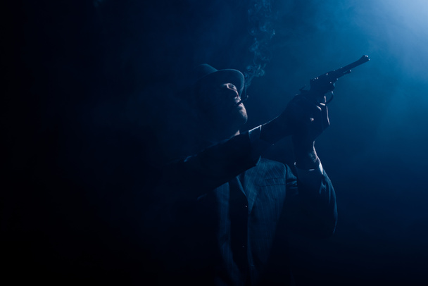 Silhouette of gangster aiming revolver and smoking on dark background - Foto, Imagem