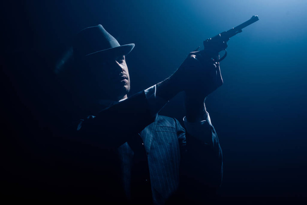 Gangster with outstretched hands aiming revolver on dark background - Photo, Image