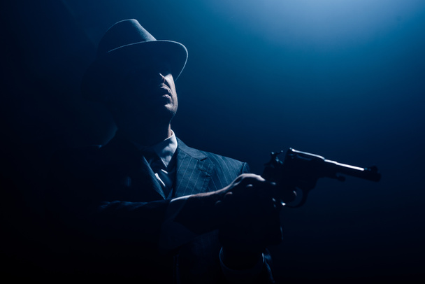 Silhouette of mafioso with outstretched hands aiming gun on dark background - Photo, Image