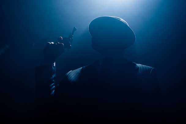 Silhouette of gangster in suit and felt hat with revolver on dark background - Zdjęcie, obraz