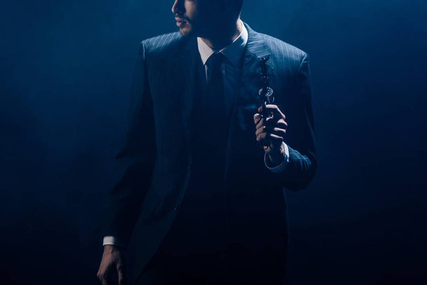 Ausgeschnittener Blick auf Gangster, der Revolver hebt und auf dunklem Hintergrund wegschaut - Foto, Bild