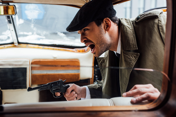 Selective focus of angry mafioso aiming gun and shouting in retro car - Фото, изображение