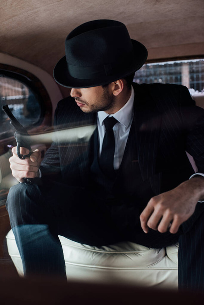 Selective focus of gangster in black suit and felt hat with gun in retro car - Foto, imagen