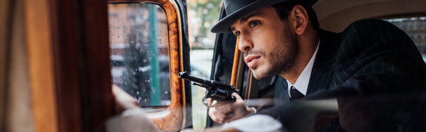 Selektywne skupienie gangstera siedzącego w zasadzce z bronią w samochodzie retro, ujęcie panoramiczne - Zdjęcie, obraz