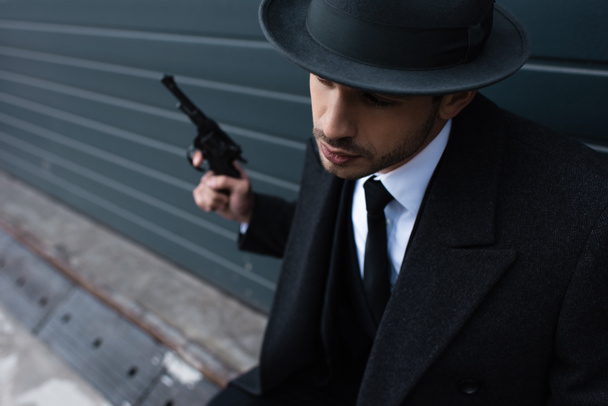 Selective focus of gangster holding revolver near wall on street - Фото, изображение