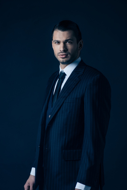 Confident mafioso in suit looking at camera on dark blue - Φωτογραφία, εικόνα