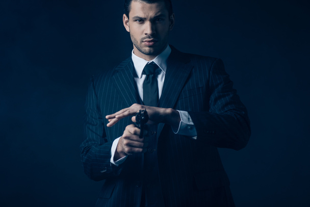 Вид спереди гангстера, нацеленного на ствол пистолета и смотрящего в камеру на темно-синем
 - Фото, изображение