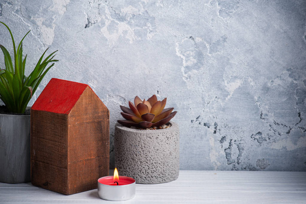 Ξύλινο σπίτι με κόκκινη στέγη και αναμμένο κερί σε ρουστίκ σύνθεση σε λευκό ξύλινο τραπέζι. Διακόσμηση σε σκανδιναβικό στυλ για ευχετήρια κάρτα με χώρο αντιγραφής - Φωτογραφία, εικόνα