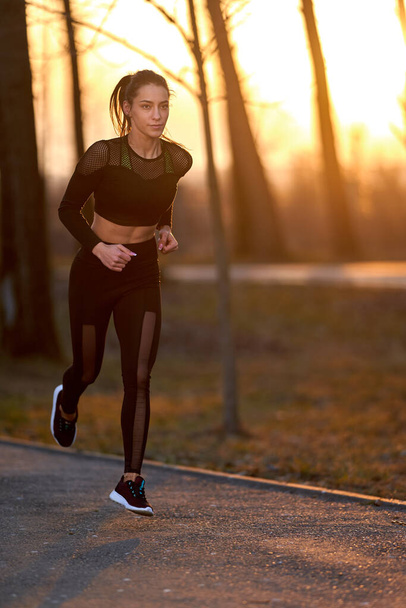 Athletic woman in track suit running in the park - Fotó, kép