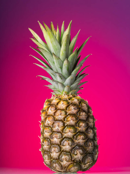 Large pineapple with peel and green leaves on pink background - Photo, image