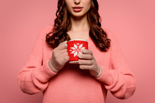 vista recortada de mujer joven en guantes sosteniendo taza de bebida caliente aislado en rosa
 - Foto, Imagen