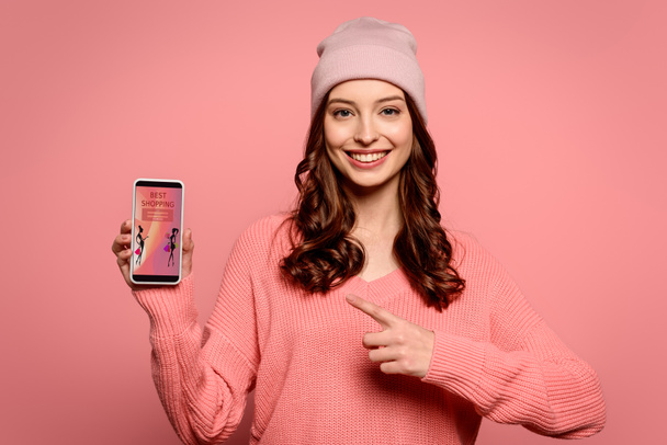 happy girl pointing with finger at smartphone with best shopping app on screen isolated on pink - Photo, Image