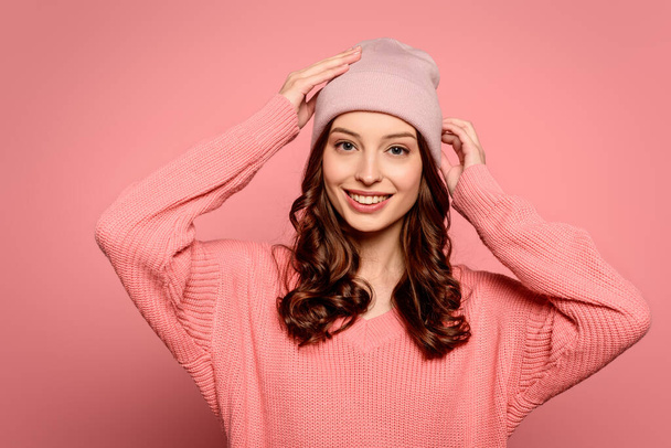 happy girl touching hat while smiling at camera on pink background - Fotoğraf, Görsel
