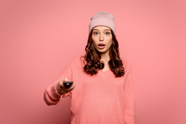 shocked girl holding tv remote controller on pink background - Photo, Image