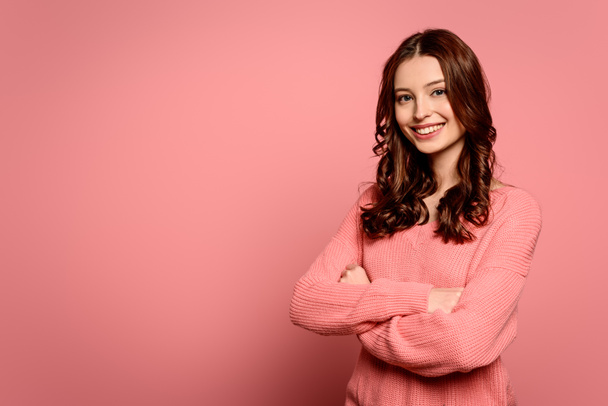 cheerful girl looking at camera while standing with crossed arms on pink background - Fotografie, Obrázek