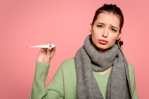 sick, displeased girl in warm showing thermometer isolated on pink - Photo, Image