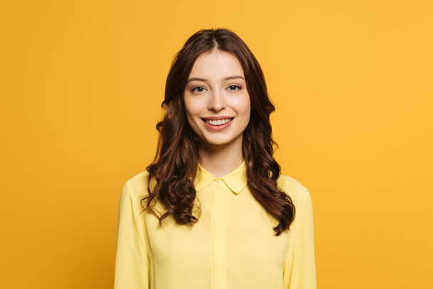 veselá dívka s dlouhými kudrnatými vlasy s úsměvem na kameru izolované na žluté - Fotografie, Obrázek