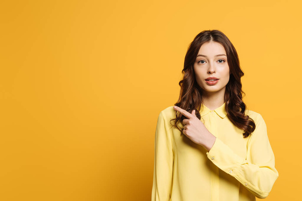 serious, attractive girl looking at camera and pointing with finger on yellow background - Foto, Imagem