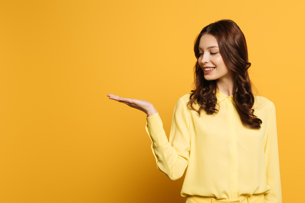 happy, attractive girl smiling while standing with open arm on yellow background - Φωτογραφία, εικόνα