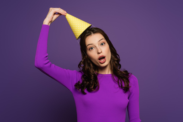 fille gaie avec bouche ouverte toucher chapeau de fête sur fond violet
 - Photo, image