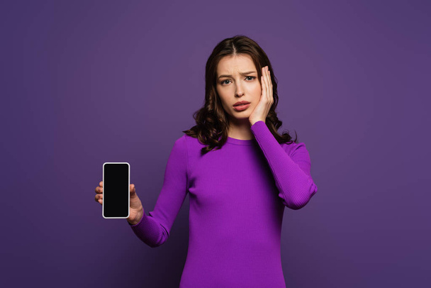 upset girl showing smartphone with blank screen on purple background - Фото, зображення