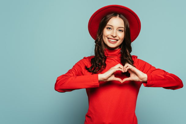 happy stylish girl showing heart symbol with hands on blue background - Foto, Imagen