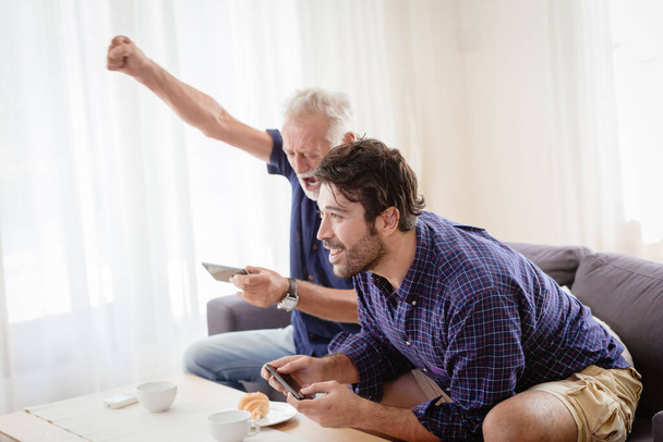 Avô mais velho feliz desfrutar momento divertido com seu filho em casa jogando jogo móvel juntos
. - Foto, Imagem