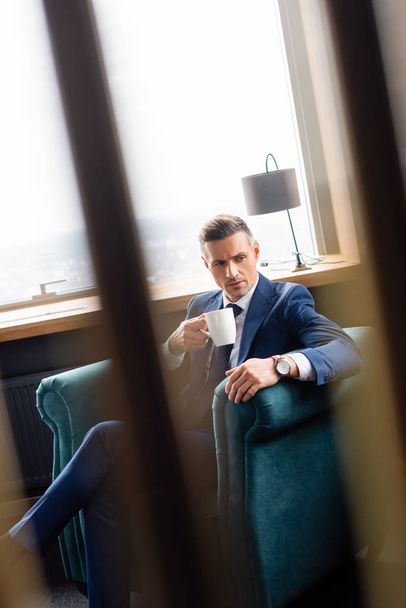 selective focus of businessman in suit holding cup and sitting in armchair  - Foto, Bild