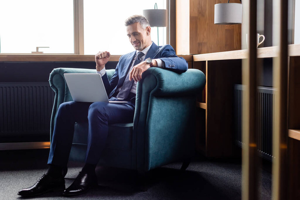 smiling businessman in suit showing yes gesture and using laptop  - Fotó, kép