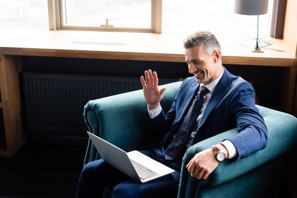 high angle view of smiling businessman in suit waving during video call  - Fotografie, Obrázek