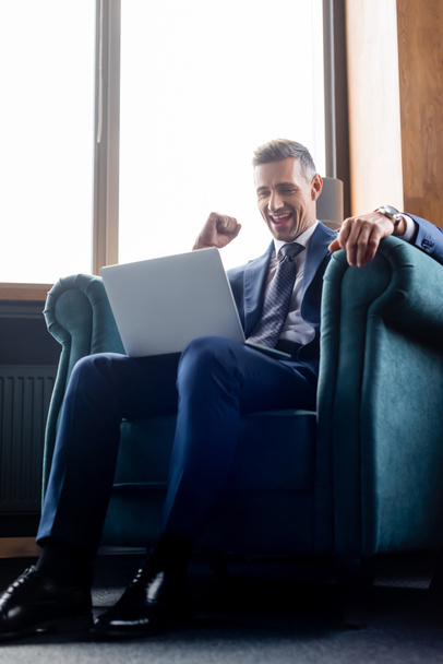 low angle view of businessman in suit using laptop and showing yes gesture  - Foto, imagen