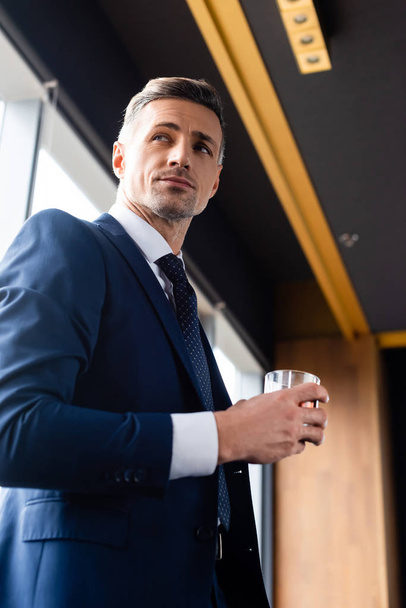 low angle view of handsome businessman in suit holding glass  - Fotó, kép