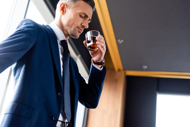 vue en angle bas de bel homme d'affaires en costume boire du cognac
 - Photo, image