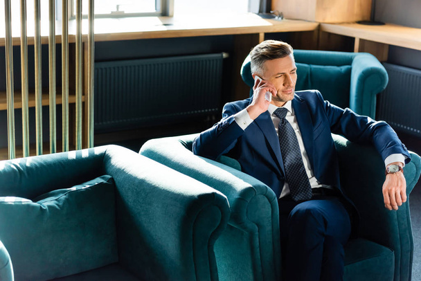 businessman in suit talking on smartphone and sitting in armchair  - Foto, Imagem
