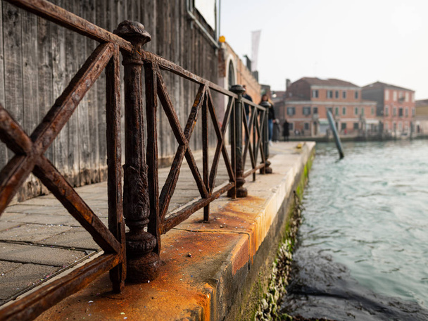 Старый ржавый забор возле канала в Мурано (Венеция, Италия)
) - Фото, изображение