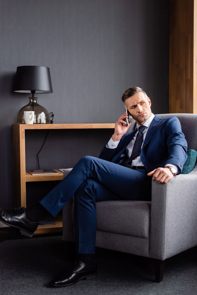 επιχειρηματίας με κοστούμι μιλάει στο smartphone και κάθεται στην πολυθρόνα  - Φωτογραφία, εικόνα