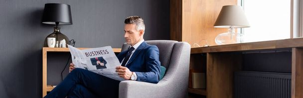 panoramic shot of businessman in suit reading newspaper with business lettering  - 写真・画像