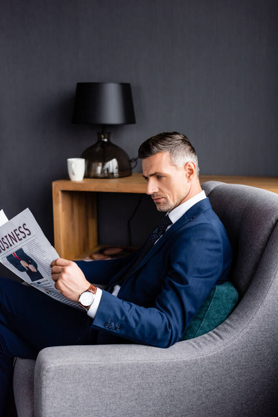 side view of businessman in suit reading newspaper with business lettering and sitting in armchair  - Photo, image