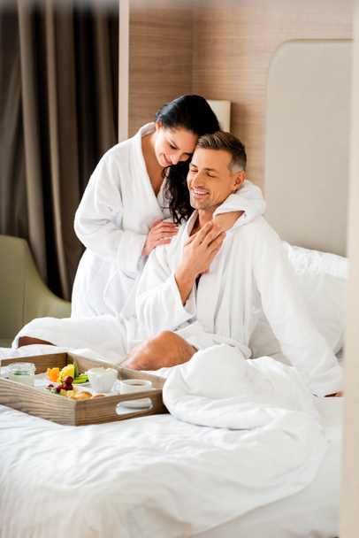 smiling girlfriend hugging boyfriend and looking at food on tray in hotel  - Foto, Imagem