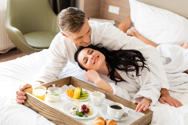 handsome boyfriend hugging smiling girlfriend near tray with food  - Fotografie, Obrázek