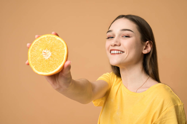 Appealing european girl shows sliced orange at the camera and smiling - Φωτογραφία, εικόνα