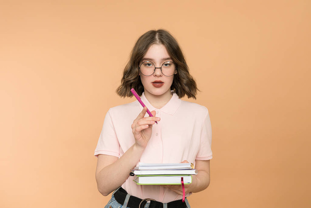 Confident young girl, student holding pen and book, notebook, love studying, reading, finished homework. Wearing ping shirt, glasses. - Foto, Bild
