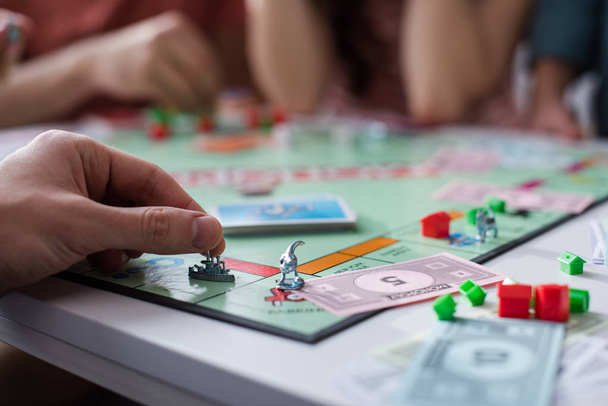 KYIV, UKRAINE - JANUARY 27, 2020: cropped view of man holding toy figurine while playing monopoly game with friends - Foto, afbeelding