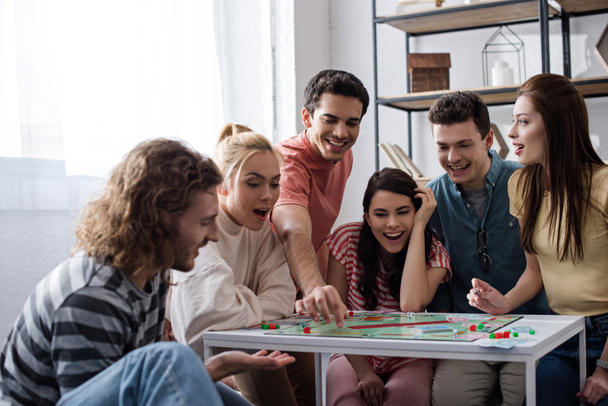 KYIV, UKRAINE - JANUARY 27, 2020: excited young friends playing monopoly game at home - Foto, imagen