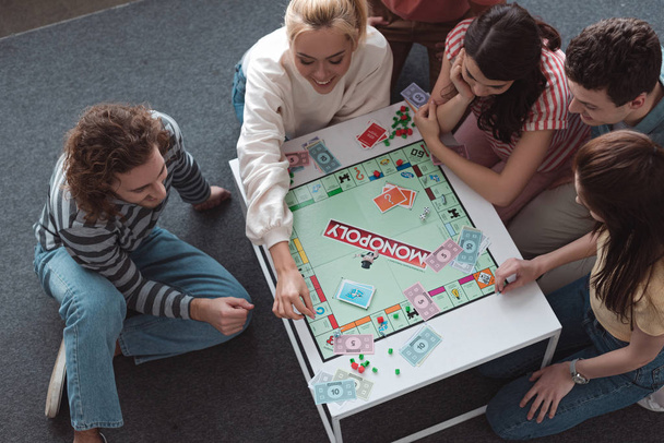 KYIV, UKRAINE - JANUARY 27, 2020: overhead view of smiling friends sitting on floor and playing monopoly game - Photo, Image