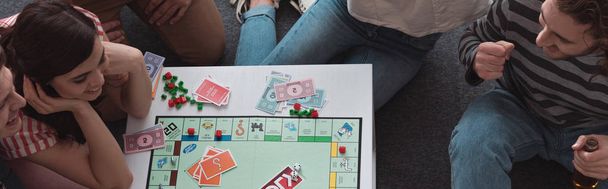 KYIV, UKRAINE - JANUARY 27, 2020: overhead view of smiling friends playing monopoly game, panoramic shot - Photo, image