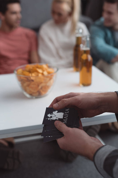 KYIV, UKRAINE - JANUARY 27, 2020: cropped view of man holding mafia game cards near table with chips and beer - 写真・画像